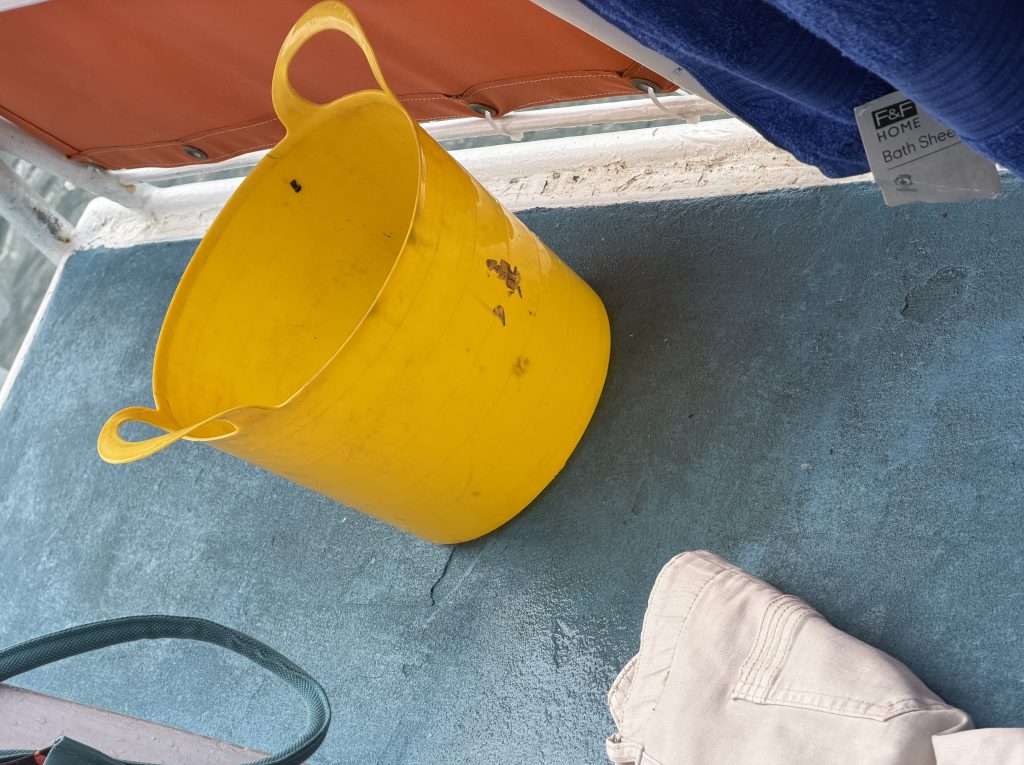 A yellow plastic bucket sitting on a gray surface, with a pair of beige pants partially visible nearby.
